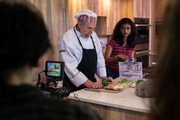 A video camera is set up to record a chef in a kitchen set.