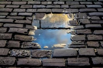 Reflection of a building in a small puddle on a brick walkway