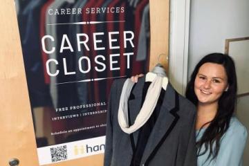 Student holding a coat in front of the door to the Career Closet