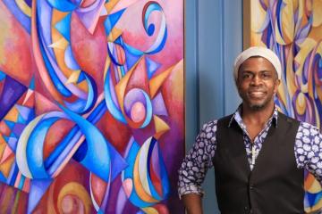 Cedric Michael Cox standing in front of one of his colorful, abstract paintings