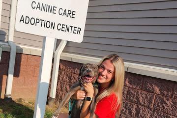Jess Mitchell holding a dog in front of a sign that says "Canine Care Adoption Center"