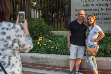 A person slightly off screen is taking a photo of a dad and daughter in front of the Ohio University Class Gateway 