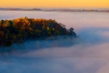 Sunrise illuminates fall colors on the hills surrounding the city of Athens, which is covered by fog near the Hocking River. 