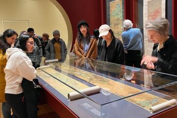 A group of people gather around a glass-encased scroll in a museum