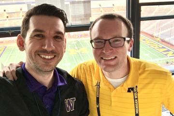 Tony Castricone and Brian Boesch  are shown in the broadcast booth at the University of Michigan football stadium in 2021