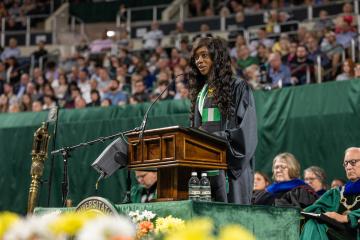 A student in a cap and gown speaks from a podium
