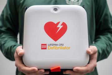 An emergency defibrillator is held by a person wearing a green Ohio University shirt
