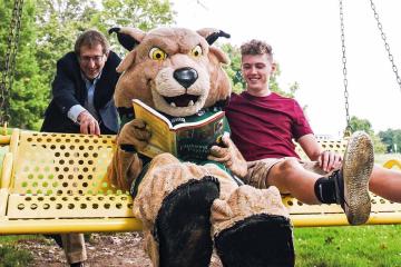 Mark Shatz and his son, Ethan Shatz, a first year, take a swing with Rufus as he studies the finer points of psychology. Photo by Ellee Achten, BSJ ’14, MA ’17