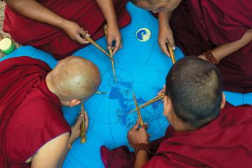 Buddhist monks work on drawing a mandala