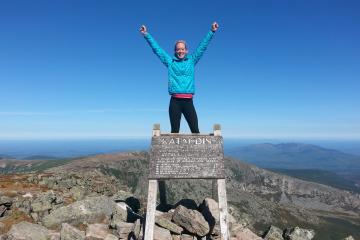 Kate Schmidlin standing triumpantly above a sign reading Mount Katahdin, Maine