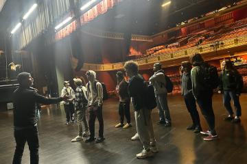 A group of students stands on a stage with their backs to the empty theater seats