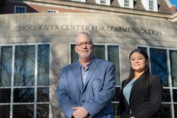 Dean Scott Titsworth poses with sophomore Bella Moyers-Chavez in front of the Schoonover Center for Communication