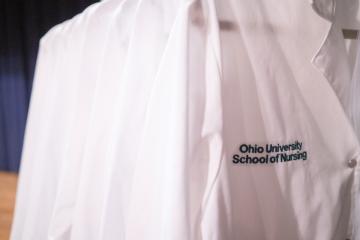 a group of white lab coats with "Ohio University College of Nursing" embroidered on the front.