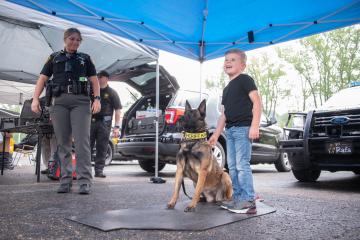 A child stands next to a police dog and a law enforcement officer at Kids and Cops Day