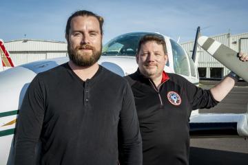 Bart Gray ’99 and Joshua Podlich ’12 stand next to Century Mission, a record-breaking flight to circumnavigate the globe