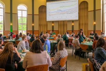 A speaker is shown talking to a large crowd of faculty and staff at the Student Success Summit in the Walter Hall Rotunda
