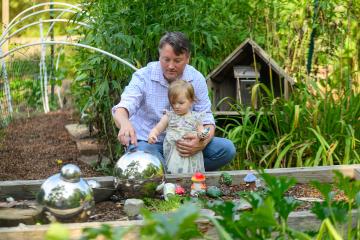 A man crouches behind a child, pointing to colorful sculptures in a garden