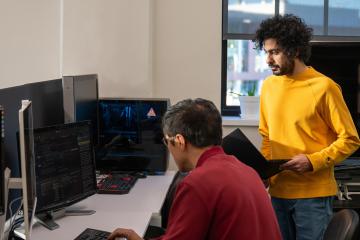 One person working on computer code as another watches, holding a laptop at Ohio University.