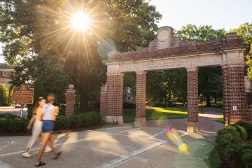 two people walk by the Alumni Gateway on a sunny morning