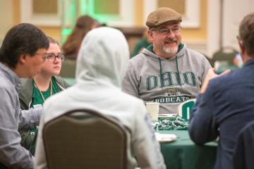 A father wearing an Ohio University sweatshirt sits with family members and others at the Pancakes with the President breakfast during Dads Weekend 2023