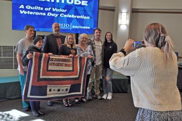 woman taking photo of seven family members behind Quilt of Valor