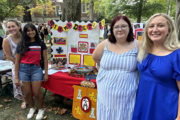 Four students pose for a photo in front of a Sigma Delta Pi poster at the student involvement fair