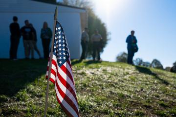 The American flag sits in the foreground, with veterans and others at the Stand Down in the background.