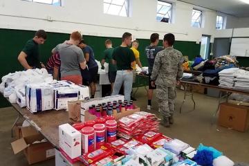Volunteers stand in the background of essential supplies to help the homeless and those in need.