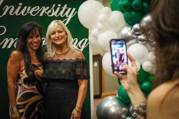 Paula Tolliver poses for a photo with a friend, while they stand near green and white balloons at the 2024 Alumni Awards Gala