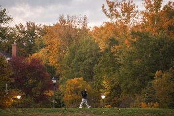A student walks on OHIO's Athens Campus on a Fall day when the trees are filled with colorful leaves