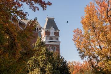 A large bird flies over a building and colorful Fall trees at The Ridges at Ohio University