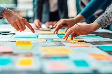 Individuals point at posted notes that are spread out on a table