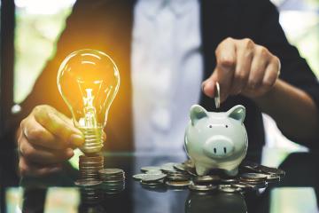 A person sorts coins into a piggy bank next to a glowing lightbulb