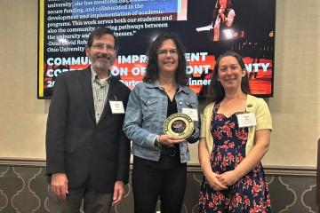 woman holding an award in center of photo featuring 3 people