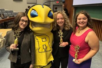 Three students pose with the Rochester mascot, a yellow bee