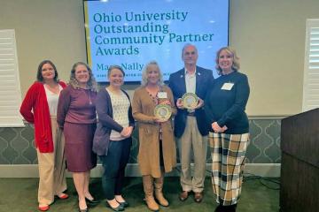 six people hold two awards at the front of a room