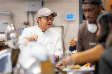 A chef is pictured at a banquet with other people serving themselves in the foreground
