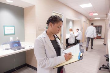 A Heritage College representative works in a medical facility while other medical professionals work nearby