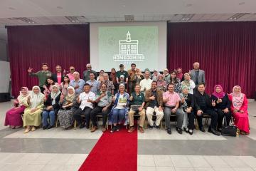 group photo of nearly 40 people celebrating OHIO's Homecoming 2024, smiling and posing in front of a maroon curtain