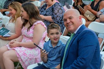 Jeremy Clay and son sitting in rows of white chairs, surrounded by others