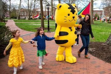 The Chubu University mascot is shown with children and an adult on the College Green during the International Street Fair