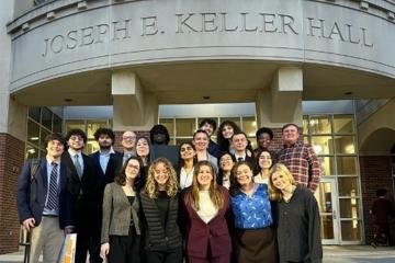 A group of students poses for a picture in front of a law school building