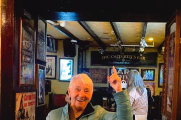 Maureen Weissenrieder, smiling, poses beneath a sign for McCafferty's Bar in Donegal Town