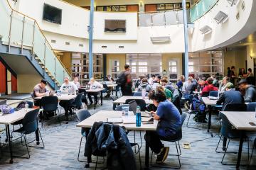 students sit at tables in a large, sunny atrium