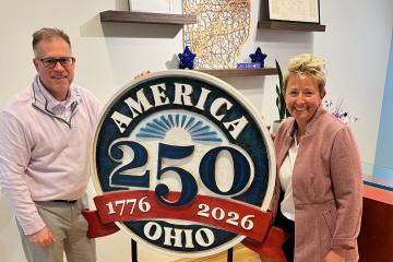 Tom Kleismit and Amista Lipot are shown with an America 250th anniversary sign
