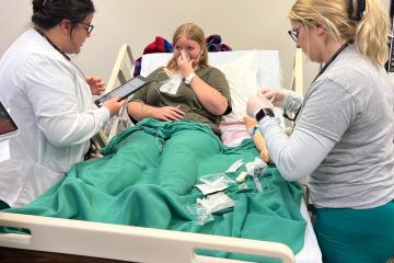 Two nursing students attend to simulation patient with breathing mask