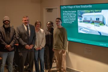 Voinovich School students and a member of the Mayors Partnership for Progress stand in front of a slide about the village of New Straitsville.