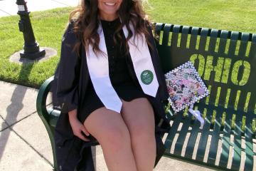 Young woman sits on bench in graduation smock