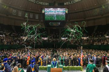 Streamers fall from the Convocation Center ceiling while  President Lori Stewart Gonzalez congratulates a large crowd of graduates at Spring Commencemenbt