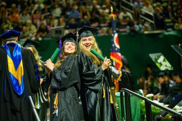 Two OHIO graduates in cap and gown celebrate after walking across the stage at Spring Commencement